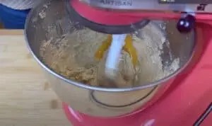 Mixer blending cookie dough with eggs in a pink stand mixer bowl.